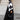 Femme en hijab géométrique noir et blanc Audacy Mimi Kiseki, en tenue noire, posant devant une architecture élégante, parisienne avec un sac structuré noir pour un look affirmé et minimaliste.