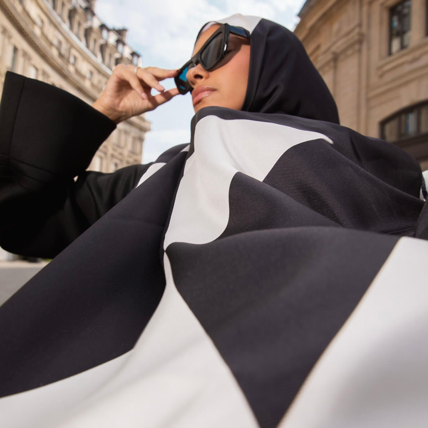Femme voilée portant le hijab Audacy Mimi Kiseki au design géométrique, dans un cadre architectural parisien, symbole d'audace et de distinction.
