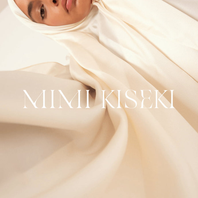 Femme portant le hijab origin écru, capturée en contre-plongée, avec le logo Mimi Kiseki en surimpression – une image forte de l’élégance, de la douceur et de l’identité visuelle de la marque.