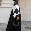 Femme en hijab géométrique noir et blanc Audacy Mimi Kiseki, en tenue noire, posant devant une architecture élégante, parisienne avec un sac structuré noir pour un look affirmé et minimaliste.