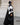 Femme en hijab géométrique noir et blanc Audacy Mimi Kiseki, en tenue noire, posant devant une architecture élégante, parisienne avec un sac structuré noir pour un look affirmé et minimaliste.