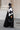 Femme en hijab géométrique noir et blanc Audacy Mimi Kiseki, en tenue noire, posant devant une architecture élégante, parisienne avec un sac structuré noir pour un look affirmé et minimaliste.