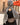Femme en hijab pied-de-poule Infinity Mimi Kiseki, photographiée de profil en extérieur, portant une abaya noire élégante et un sac arrondi beige, style raffiné et urbain.